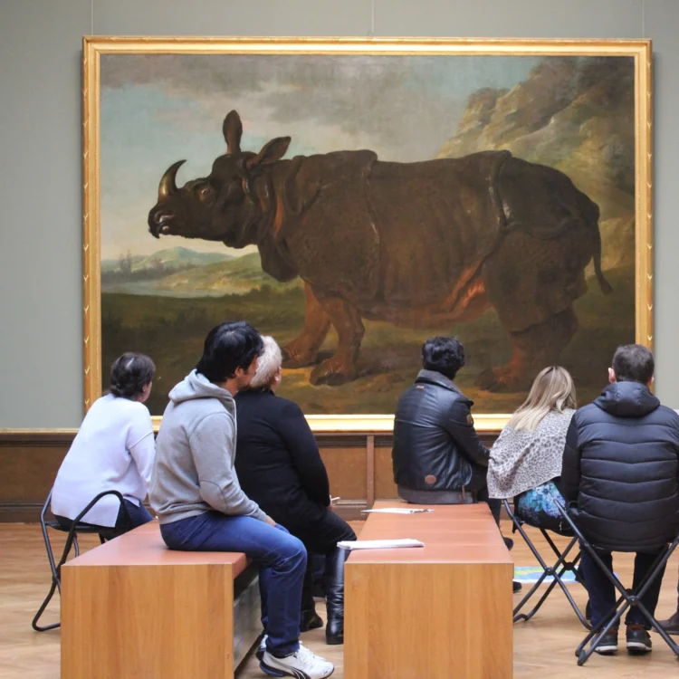 Menschen sitzen im Museum vor dem Bild eines Nashornes